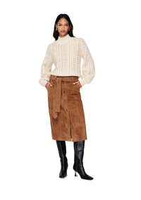 Woman wearing a white ribbed sweater, brown corduroy skirt, and black knee-high boots on a white background