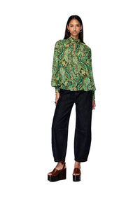 Woman wearing a green patterned blouse and black pants on a white background