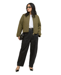 Woman wearing an olive green quilted jacket and dark pants on a white background