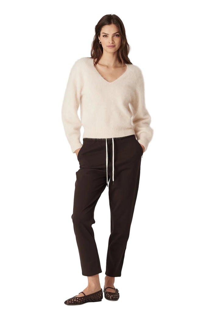 Woman wearing a cream sweater and black pants on a white background