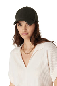 Woman wearing a black cap and white top with a gold necklace on a light background