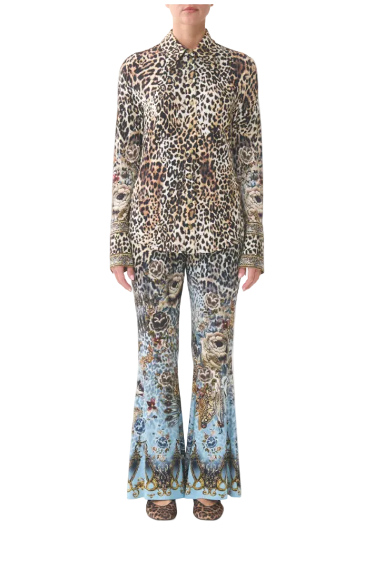 A model wearing a matching two-piece suit set consisting of a long-sleeve button-up shirt and wide-leg trousers, both featuring a mixed animal print pattern with leopard spots and blue/gold floral motifs, set against a plain light gray background.