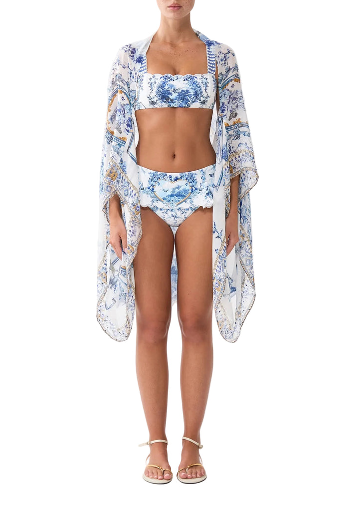 A model wearing a three-piece swimwear set featuring a blue and white floral print. The set includes a bikini with a square neckline, matching bikini bottoms, and a sheer, long-sleeve kaftan cover-up draped over the body.