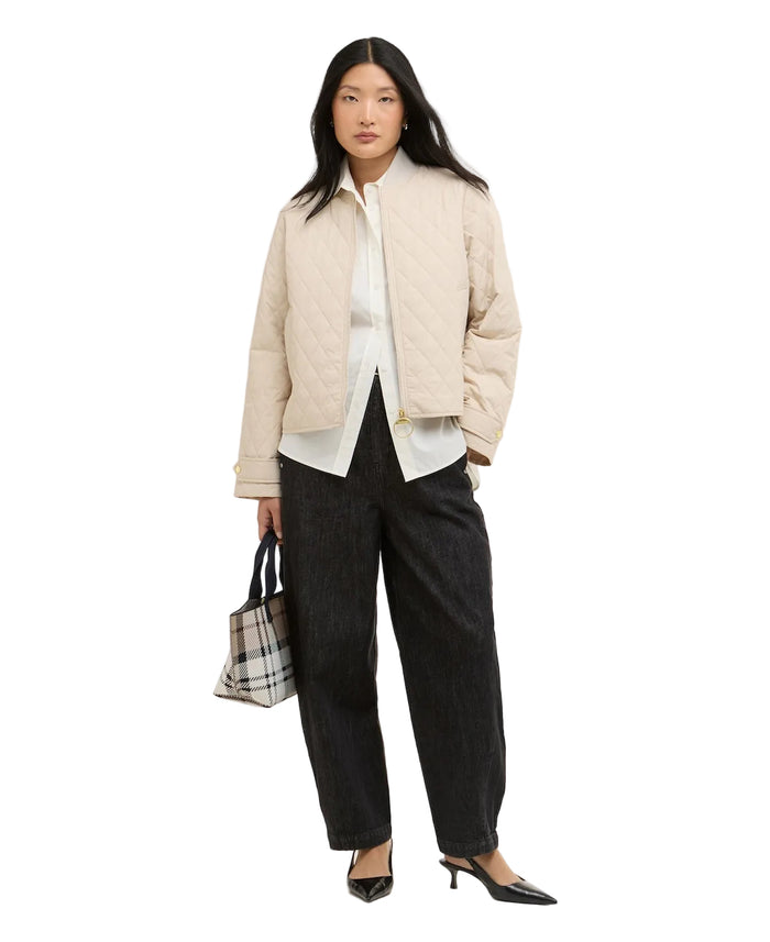 Woman wearing a beige puffer jacket, white shirt, black pants, and holding a plaid bag on a white background