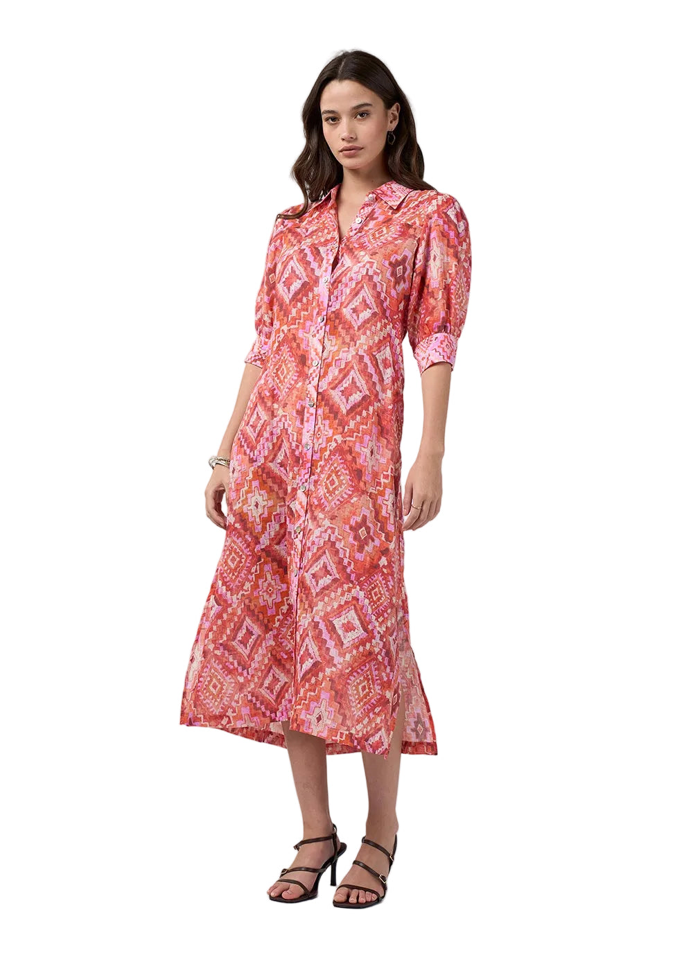A woman modeling a pink and red patterned midi shirt dress with three-quarter sleeves and a collared neckline, paired with black strappy heels against a light gray studio background.