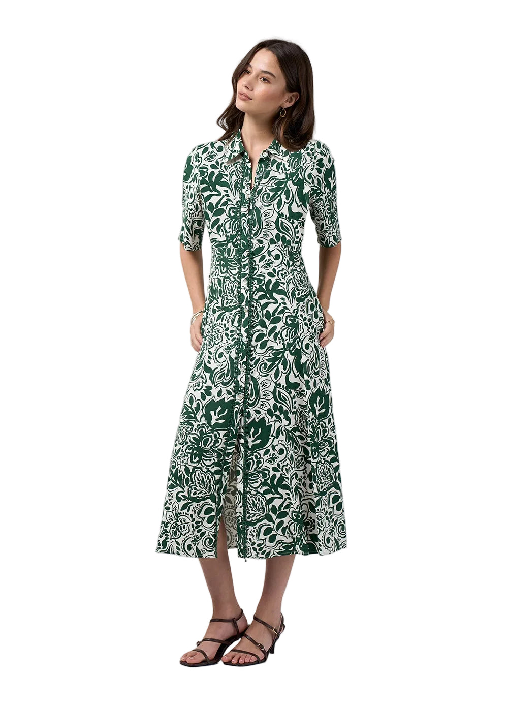 A woman modeling a green and white botanical print midi dress with short sleeves, a button-up front, and a side slit, paired with black strappy sandals against a light gray studio background.