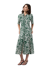 A woman modeling a green and white botanical print midi dress with short sleeves, a button-up front, and a side slit, paired with black strappy sandals against a light gray studio background.