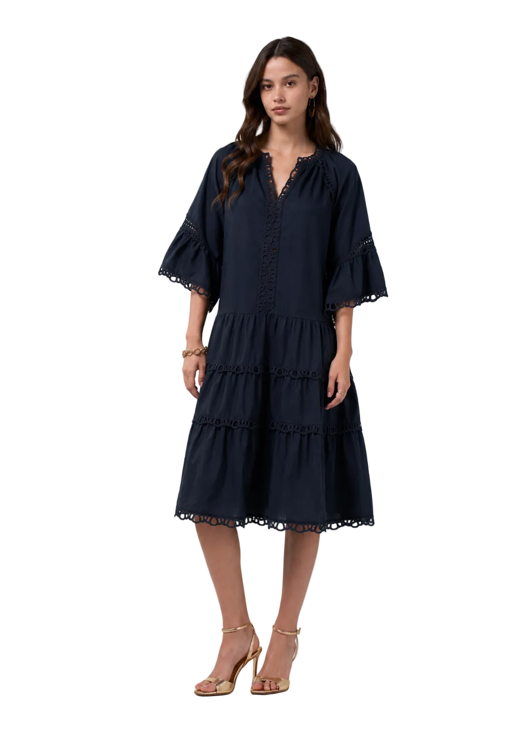 A woman modeling a dark navy blue tiered midi dress with ruffled sleeves and lace trim, paired with gold high-heeled sandals, against a light gray studio background.