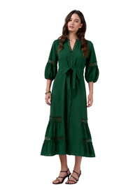A woman modeling a dark green midi dress with three-quarter puff sleeves, a matching waist tie, and decorative embroidered details on the cuffs and hem, paired with black strappy heels against a light gray studio background.