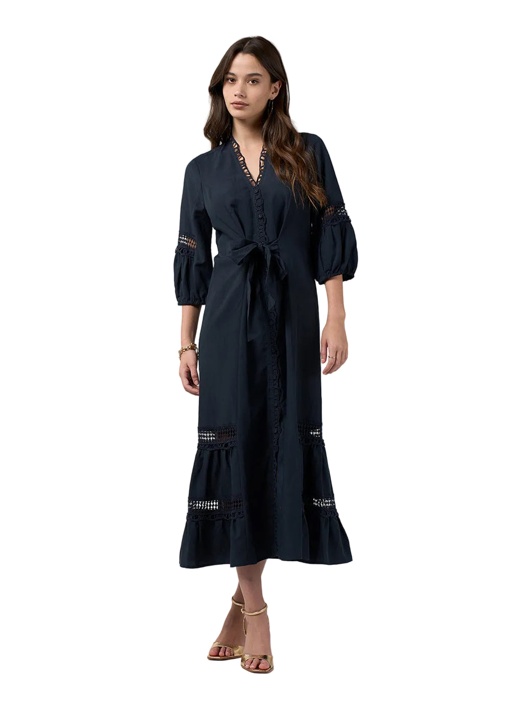 A woman modeling a dark navy midi wrap dress with puff sleeves, lace trim details, and a tie waist, set against a plain light gray studio background.