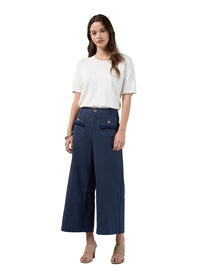 A woman modeling a pair of dark navy blue wide-leg cropped pants with front flap pockets, styled with a white short-sleeve t-shirt and beige heeled sandals against a light gray studio background.