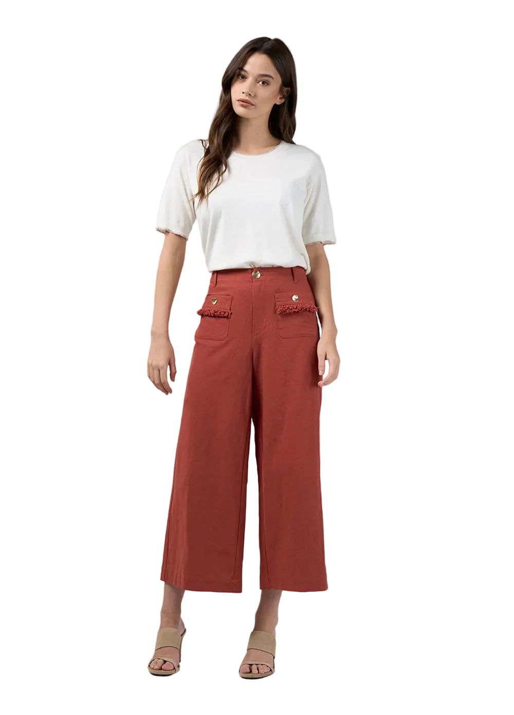 A woman modeling a white short-sleeve t-shirt and rust-colored cropped wide-leg pants with decorative flap pockets, paired with beige heeled sandals, against a light gray studio background.