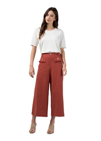 A woman modeling a white short-sleeve t-shirt and rust-colored cropped wide-leg pants with decorative flap pockets, paired with beige heeled sandals, against a light gray studio background.