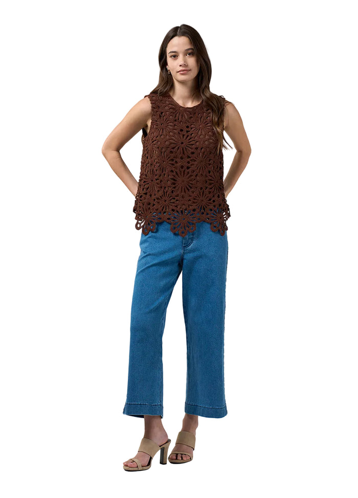 A woman modeling a brown sleeveless crochet knit top with a scalloped hem, paired with blue cropped jeans and beige heeled sandals, against a light gray studio background.