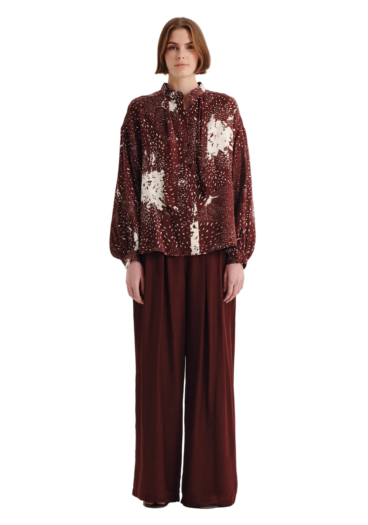 Woman wearing a patterned blouse and brown pants on a white background