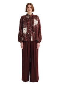 Woman wearing a patterned blouse and brown pants on a white background