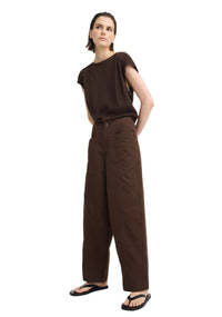 A model wearing a dark brown short-sleeve top and matching dark brown wide-leg trousers, paired with black flip-flop sandals, against a plain light gray studio background.
