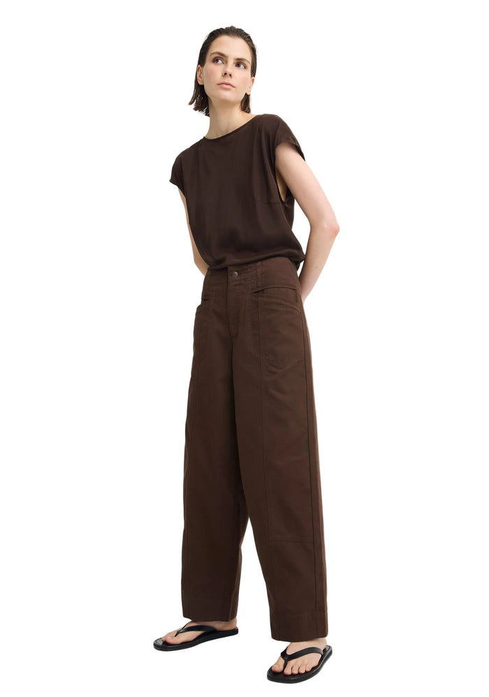 A model wearing a dark brown short-sleeve top and matching dark brown wide-leg trousers, paired with black flip-flop sandals, against a plain light gray studio background.