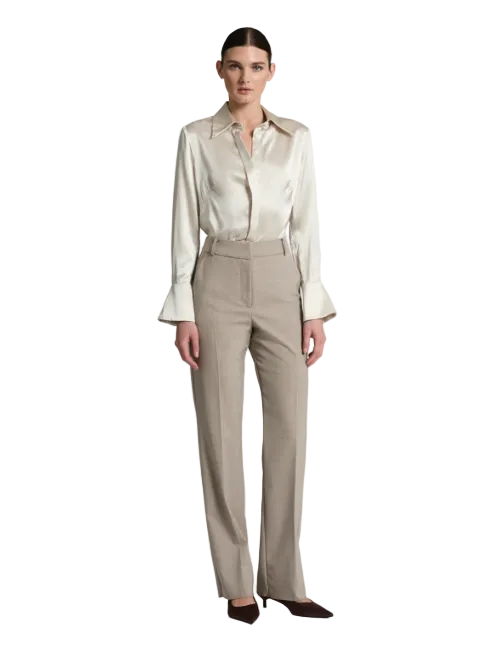 A model stands against a light gray studio background wearing a cream satin long-sleeve blouse with flared cuffs and matching beige tailored trousers, paired with dark pointed shoes.