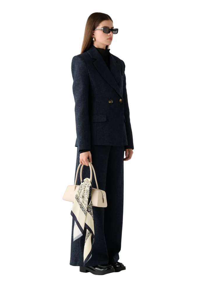 Woman in a dark suit holding a bag and scarf on a white background