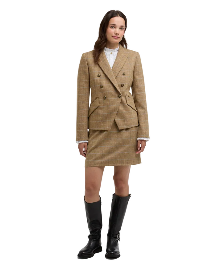 A model stands against a light gray studio background wearing a beige plaid double-breasted blazer and matching mini skirt with a white collared shirt underneath and black knee-high boots.