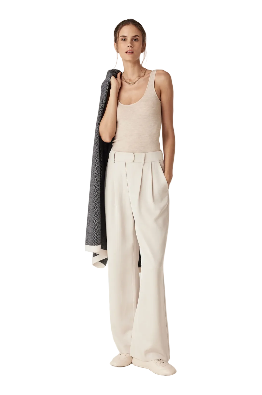 Woman wearing a beige tank top and white pants against a plain background