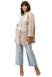 A woman modeling a light beige oversized knit cardigan with large front pockets and gold-tone buttons, paired with light blue wide-leg jeans and tan ankle boots, against a plain white studio background.